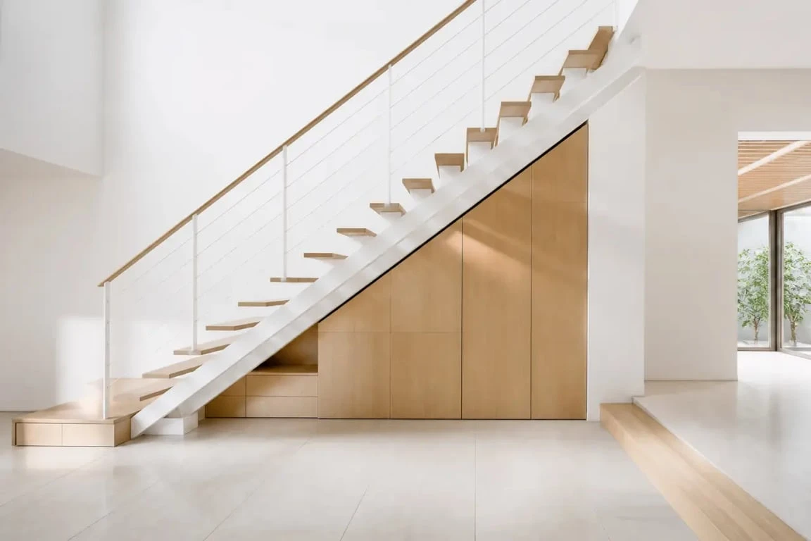 Aménagement sous escalier ouvert avec rangements bas en bois clair dans une entrée lumineuse